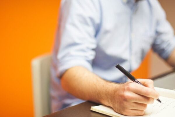 employee writing on a notebook while using a laptop